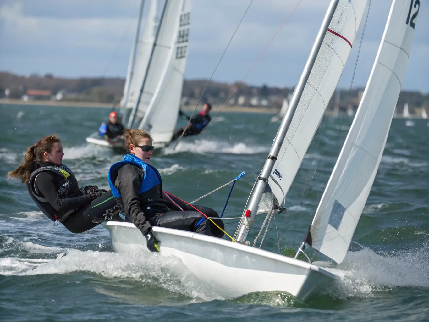 An image of a group of adults participating in an advanced sailing course, navigating through challenging waters with expert guidance from instructors. The scene showcases the skill and precision required for advanced sailing.